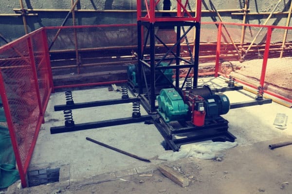 Construction site with machinery, scaffolding, and hoist installation.