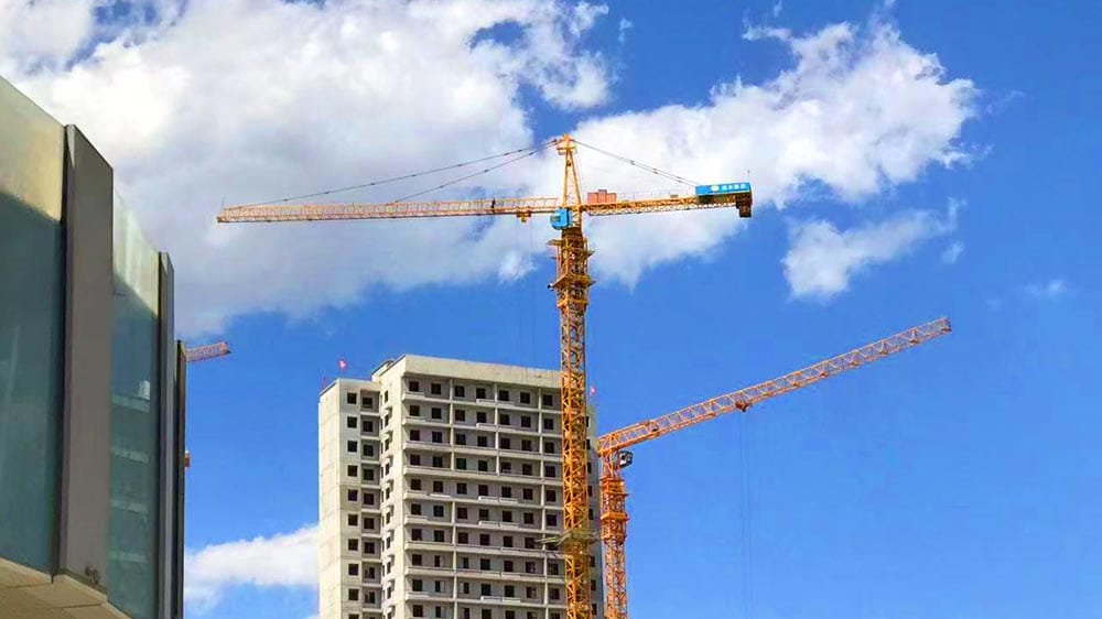 Una grúa de construcción se eleva sobre un edificio de varios pisos parcialmente construido contra un cielo azul claro con nubes.