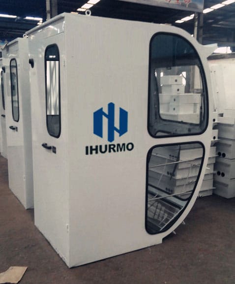 A white IHURMO-branded cabin with large windows is displayed indoors, alongside other similar cabins in the background.