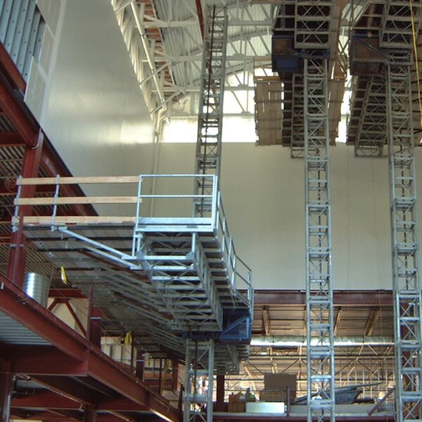 Industrial mezzanine with IHURMO single-mast mast climber and steel structures inside a warehouse.