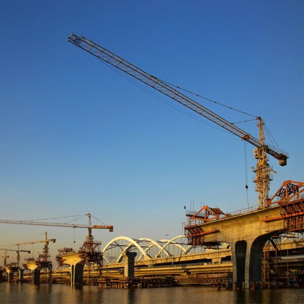 Canteiro de obras com guindastes de torre de construção IHURMO de 45m de altura e 60m de lança 6t 8t qtz100 6013 perto de uma ponte ao entardecer.