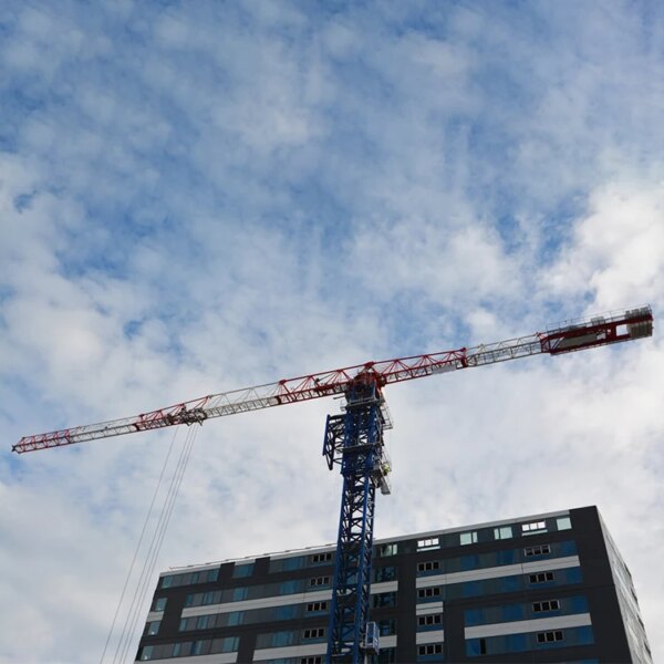 IHURMO pt7015-10 10 Tonnen Turmdrehkran mit 70 m Auslegerlänge ragt über einem modernen Gebäude vor einem bewölkten Himmel auf.