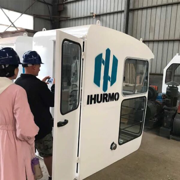 Twee personen inspecteren de cabine van een IHURMO QTZ160 TC6024 10-tons torenkraan met het logo "ihurmo" op de deur.