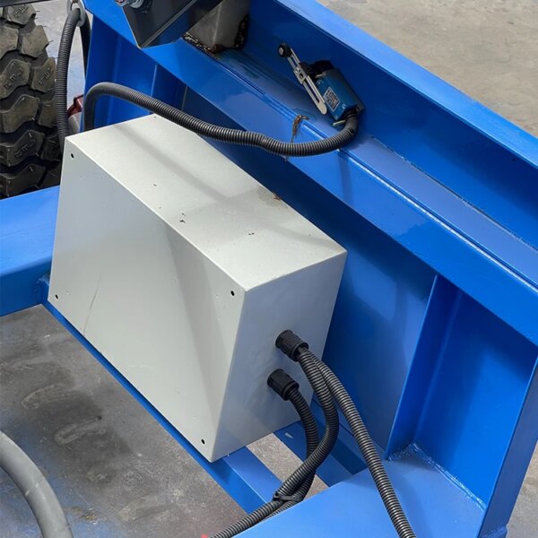 Caja de conexiones eléctricas montada sobre una superficie de metal azul con tuberías conectadas, accesible mediante un elevador de tijera IHURMO de 500 kg y 40 pies.