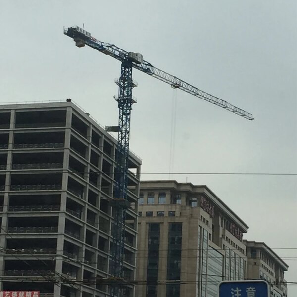 Guindaste de torre de construção plana IHURMO de 60 m, 75 m, 80 m e 100 m de altura em um canteiro de obras com edifícios ao fundo.