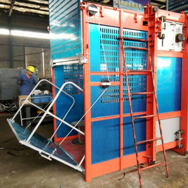 Seorang pekerja mengamati Lift Konstruksi Kandang Ganda 2*2000 kg dengan pelindung pengaman berwarna biru di bengkel manufaktur.