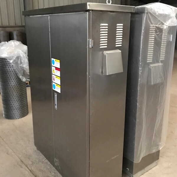 Une armoire électrique en acier inoxydable avec des étiquettes d'avertissement, enveloppée dans du plastique protecteur, conçue pour être installée à l'aide d'une grue à tour topless IHURMO pt7015-10 de 10 tonnes et d'une longueur de flèche de 70 m.