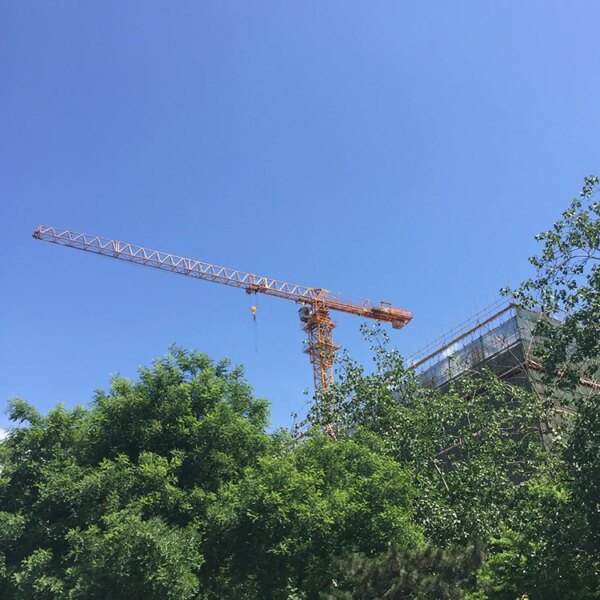 IHURMO topless tower crane for sale towering above trees against a clear blue sky.