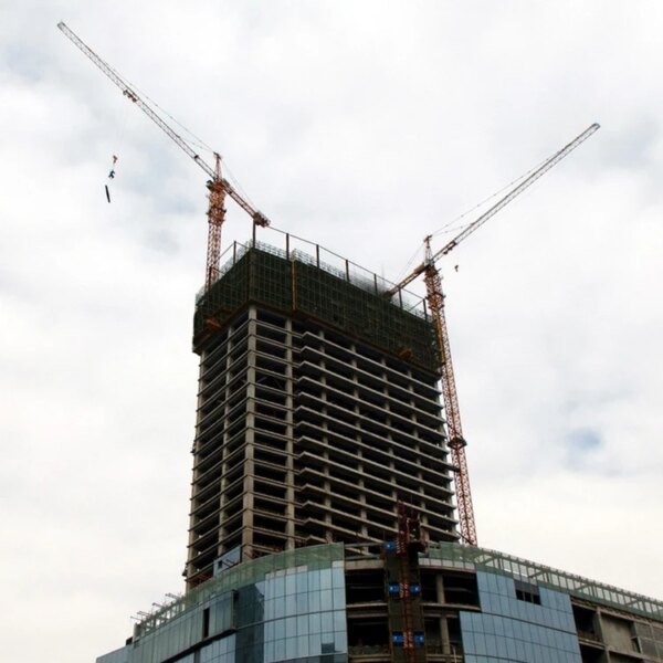 Skyscraper under construction with an IHURMO china self-raising Qtz80 5613 6T construction hammerhead tower crane for sale against a cloudy sky.