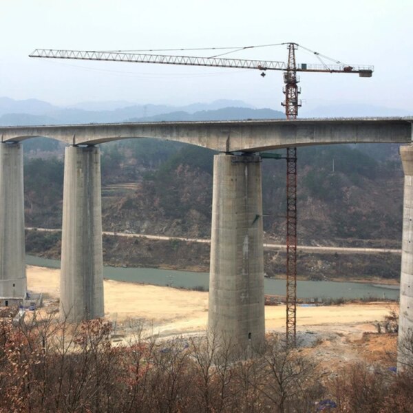 Pilares de puente sin terminar con una grúa torre IHURMO de 45 m de altura y 60 m de longitud de pluma QTZ80 TC6010 de 8 toneladas en la parte superior contra un paisaje árido.