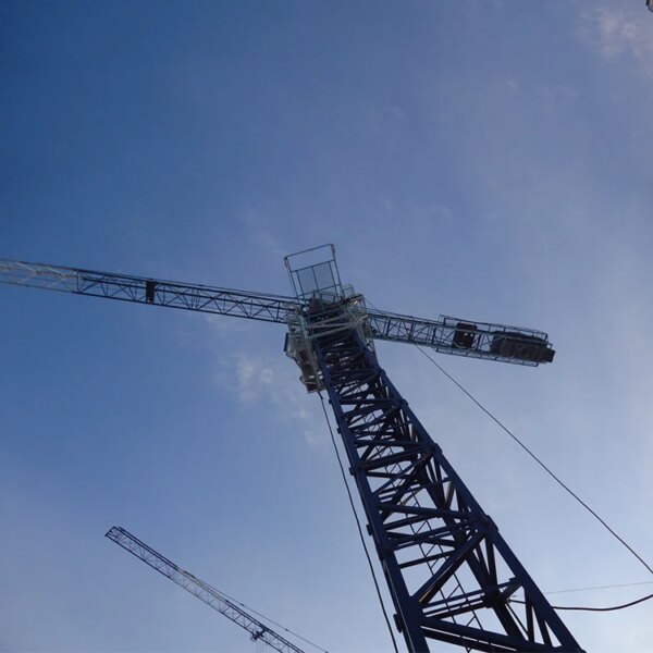 Vista en ángulo bajo de una grúa torre en topless de ingeniería de construcción de 16 toneladas de longitud de pluma IHURMO 75 de China contra un cielo despejado.