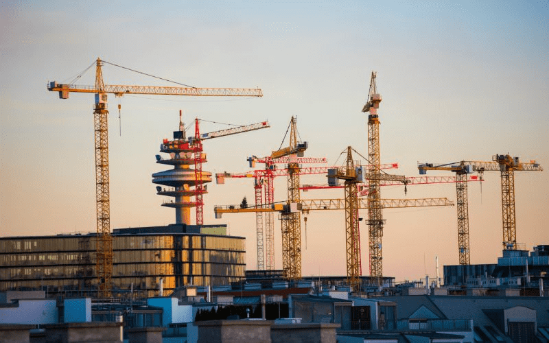 Verschillende bouwkranen torenen hoog uit boven een wolkenkrabber tegen de schemerige hemel.