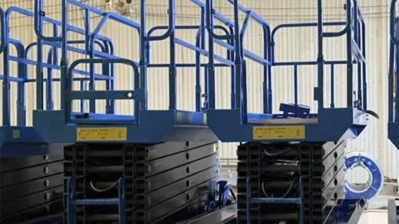 Blaue hydraulische Scherenhebebühnen mit hoher Tragfähigkeit stehen Seite an Seite in einer Halle mit großen Fenstern.