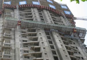 Construcción de gran altura con escaladores de mástiles y grúas IHURMO; carteles con caracteres chinos en la parte superior.