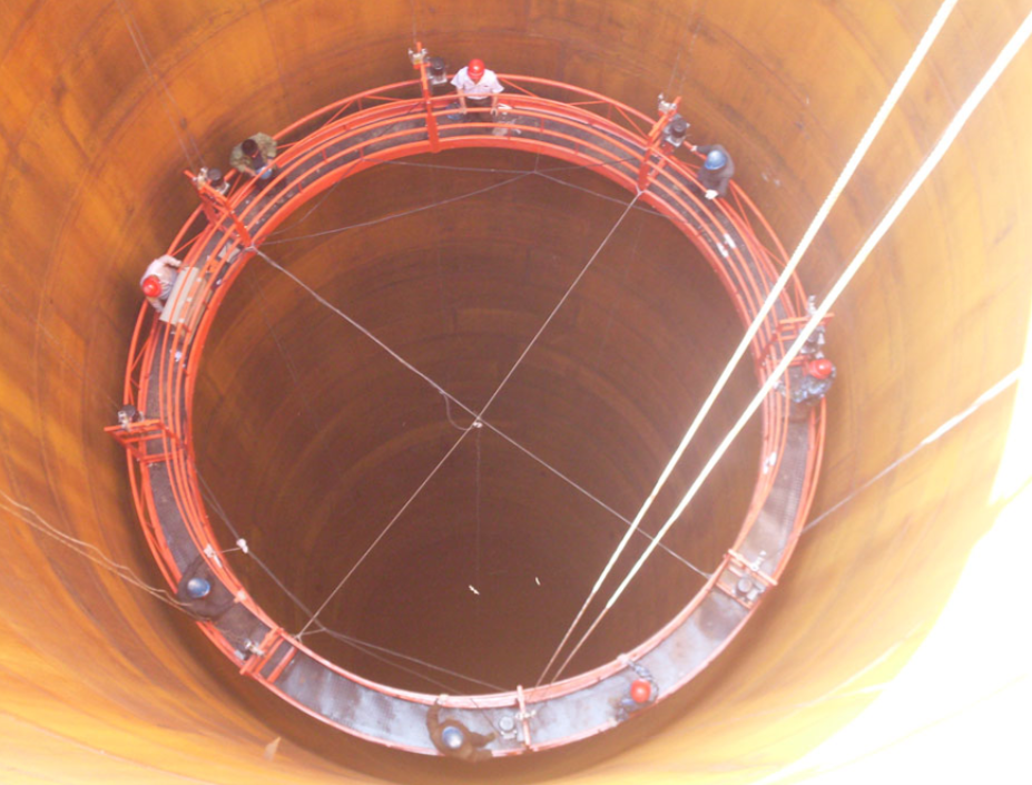 Workers sit on a circular scaffolding platform inside a large metal cylinder with cables hanging from the top, showcasing common construction setups.