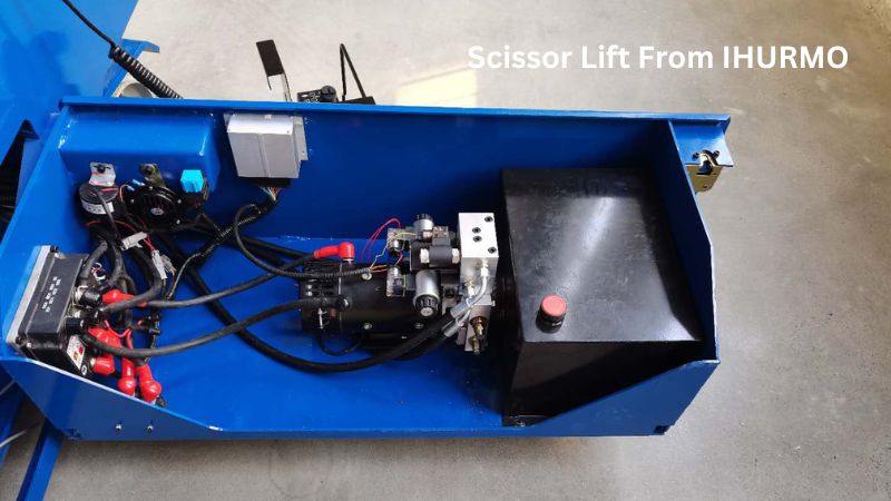 Primer plano de una plataforma elevadora de tijera azul con cables, sistema hidráulico y depósito de líquido. Texto: "Plataforma elevadora de tijera IHURMO. Evite problemas".