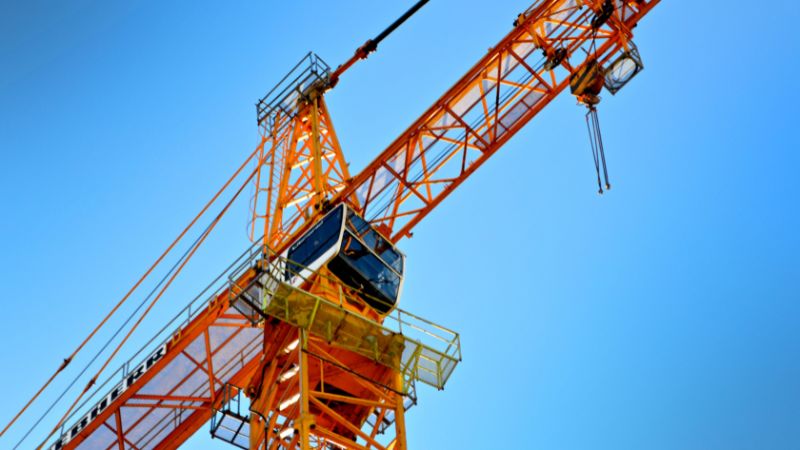 Close-up de um guindaste de construção amarelo contra um céu azul, ilustrando termos do glossário de guindastes.