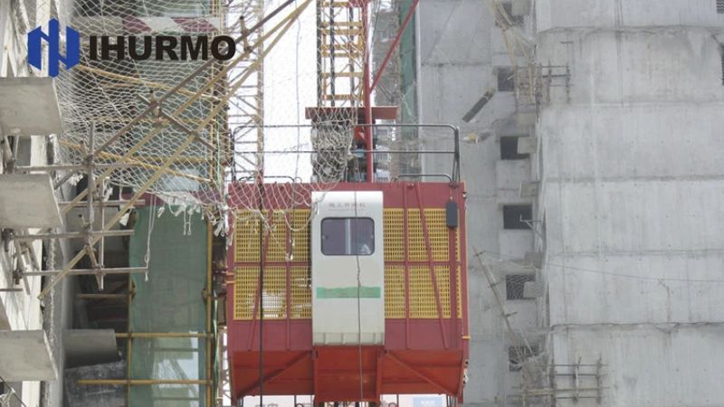 Un elevatore a cremagliera, supportato da IHURMO, garantisce un trasporto sicuro ed efficiente nel trafficato cantiere con reti e impalcature.