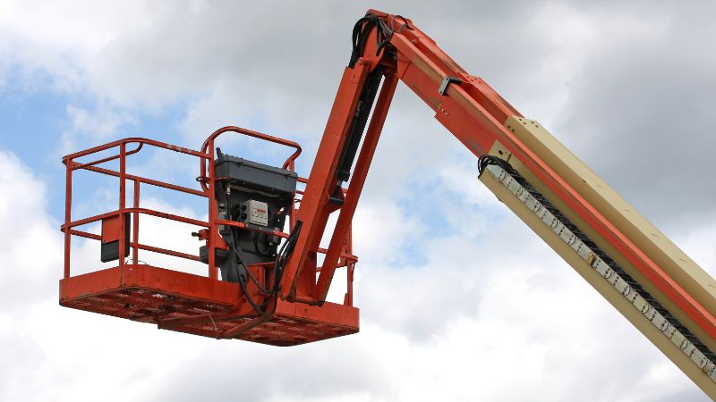 Una plataforma elevadora roja IHURMO levanta proyectos hacia el cielo bajo las nubes.