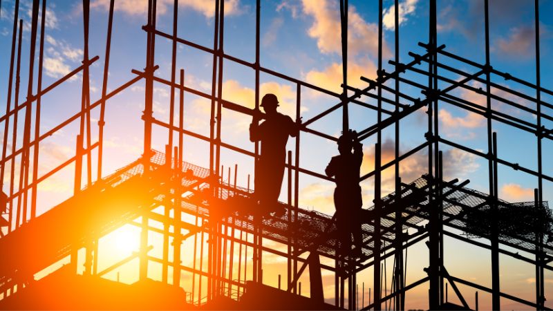 Construction workers silhouetted on scaffolding at sunset create a striking image.