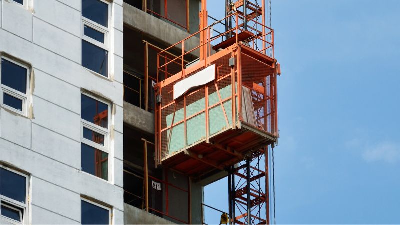 Um elevador de construção opera com segurança em um arranha-céu, ressaltando a necessidade da Lista de Verificação de Elevadores IHURMO em um céu azul.