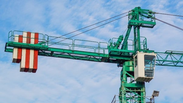 Sebuah derek menara IHURMO berwarna hijau, dengan kabin dan pemberatnya, tampak menonjol di tengah langit biru yang cerah.