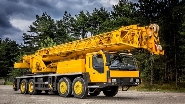 Une grue jaune IHURMO est garée sur le trottoir avec une forêt en arrière-plan sous un ciel nuageux.