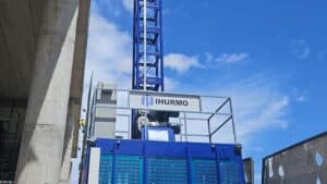 পরিষ্কার আকাশের নিচে একটি ভবনের পাশে অবস্থিত একটি নীল "HURMO" নির্মাণ লিফটে উন্নত উত্তোলন সরঞ্জামের ছবি দেখা যাচ্ছে।