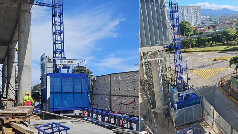Werknemers met veiligheidsuitrusting lopen rond op de steiger op een bouwplaats met een blauwe lift, tegen de achtergrond van de skyline van de stad.