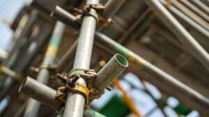 Close-up of metal scaffolding with interconnected pipes and clamps, following the 3 to 1 Rule. Blurred background highlights safety.