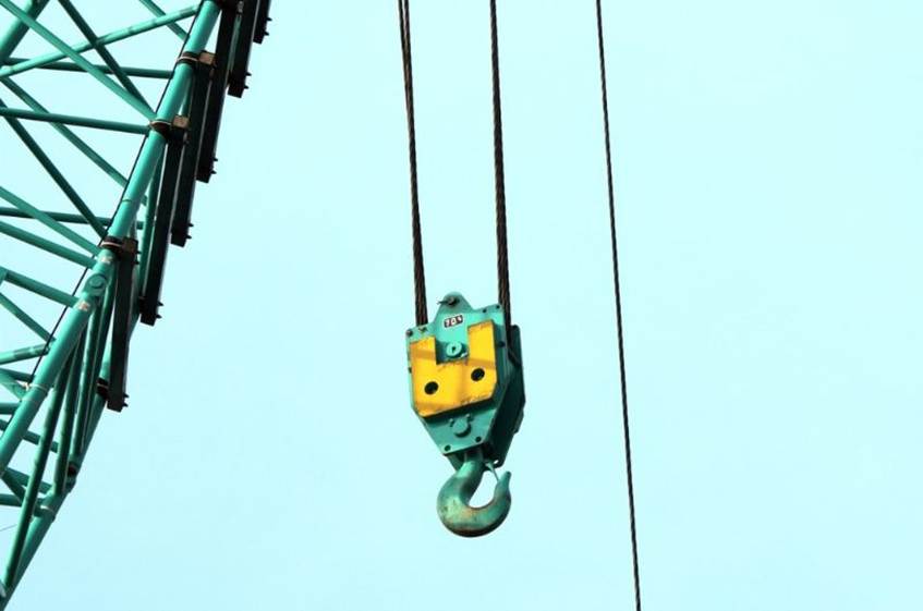 Close-up of a crane hook hanging by steel cables against a clear blue sky.