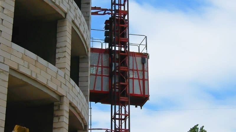 Un monte-matériaux sur un bâtiment en béton partiellement construit se détache sur un ciel bleu clair.