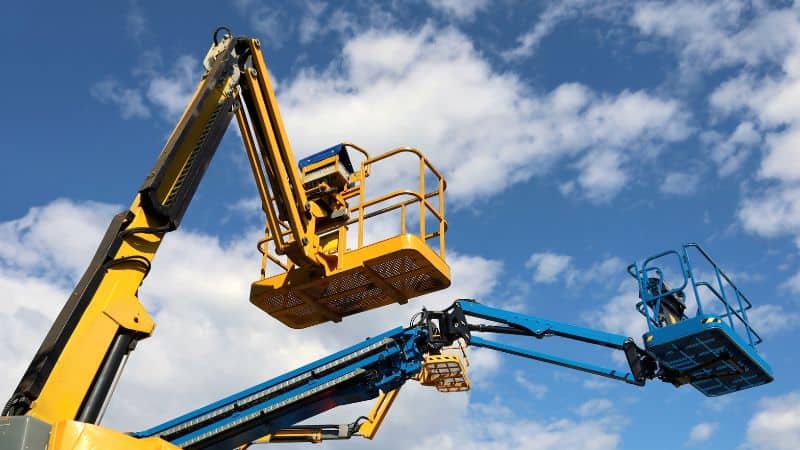 Geel-blauwe hoogwerkers steken hun platforms uit tegen een gedeeltelijk bewolkte blauwe lucht.