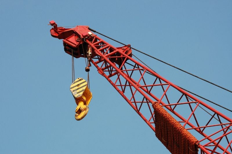 Close-up of a red crane with a striped yellow hook hanging against a clear blue sky.