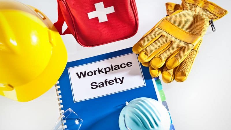Safety gear and first aid kit arranged around a blue OSHA workplace safety manual.