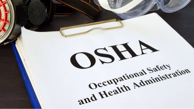 Clipboard with an "OSHA Occupational Safety and Health Administration" document and safety gear in the background.