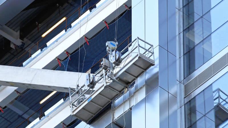 A suspended platform beside a glass building, likely for window cleaning, follows OSHA scaffolding safety standards.