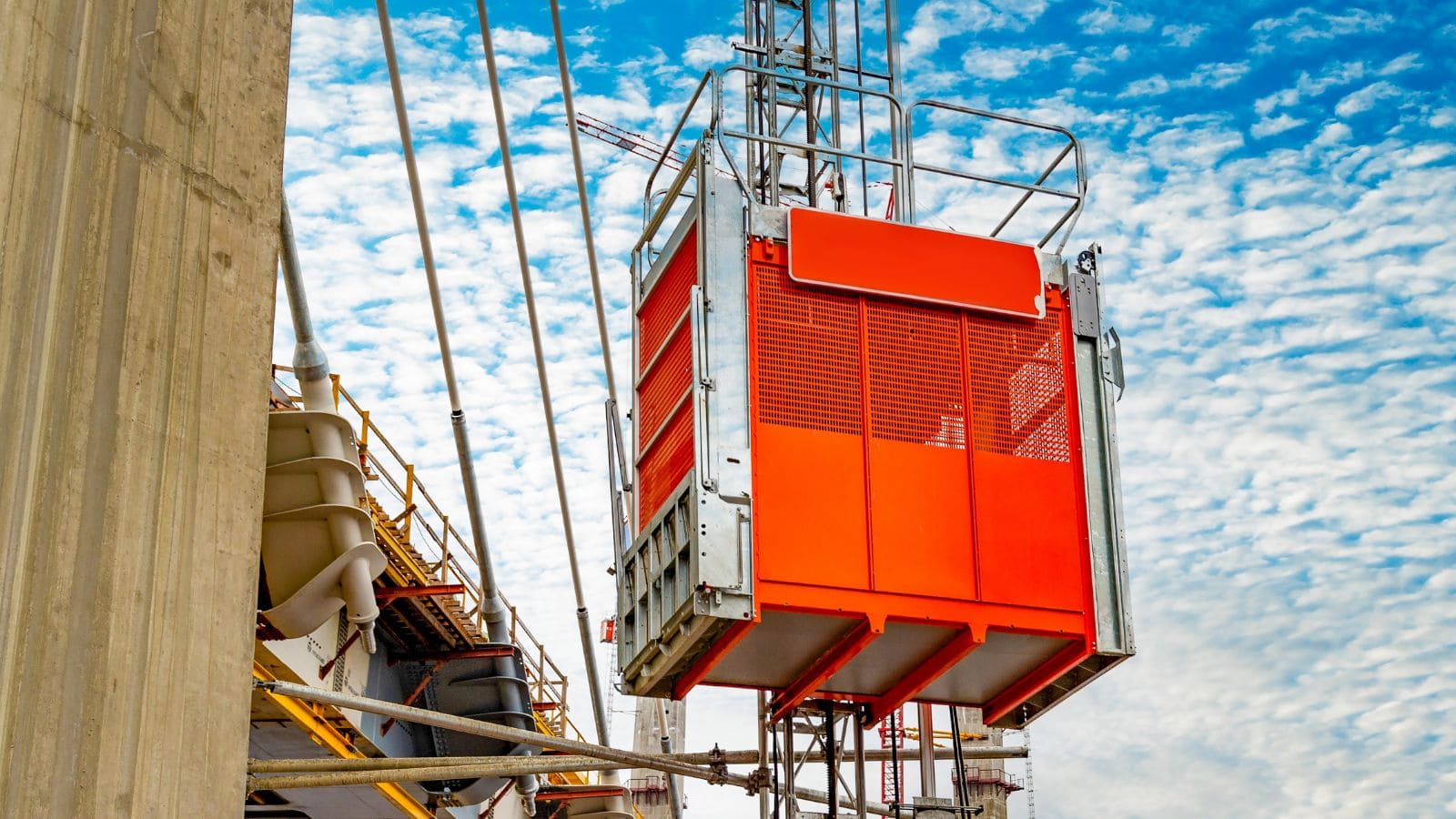 Construction hoist with safety cage on a high-rise building under blue sky, used for transporting workers and materials.