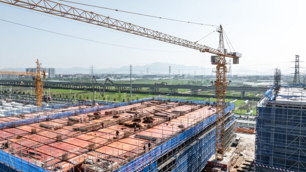 Large tower crane operating at a construction site with building framework and scaffolding, highlighting construction equipment and infrastructure development.