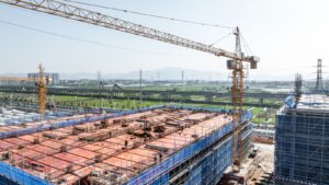 Large tower crane operating at a construction site with building framework and scaffolding, highlighting construction equipment and infrastructure development.