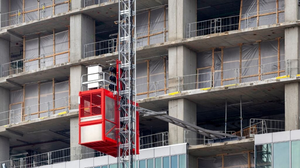 Construction hoist with safety features on a high-rise building under construction, emphasizing site controls for safety.