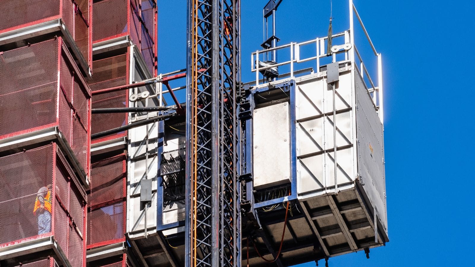 Construction hoist safety cage with site controls at a construction site, emphasizing safety measures to prevent failures.