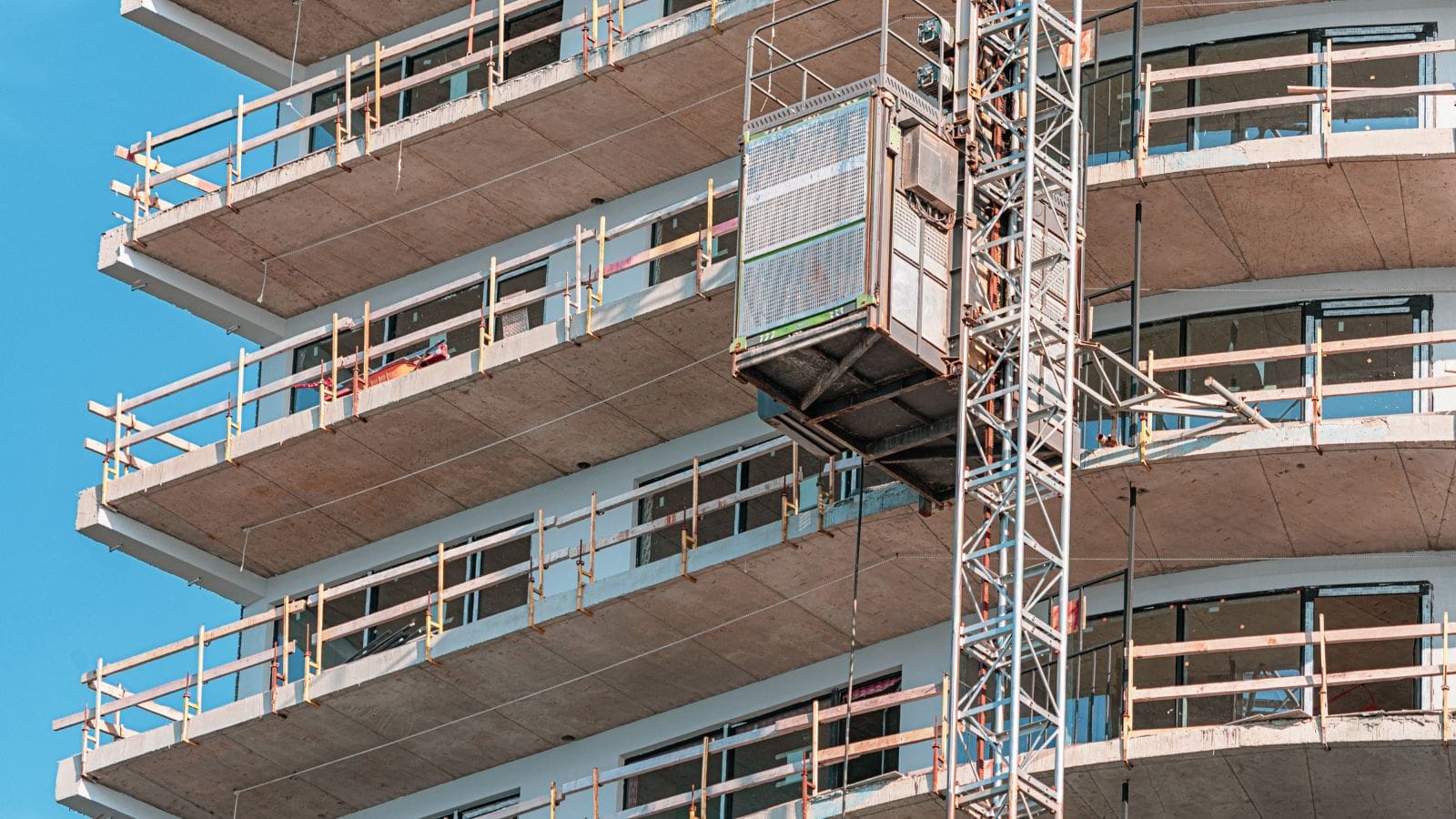 Close-up of a construction hoist with safety barriers and site controls on a high-rise building under construction.