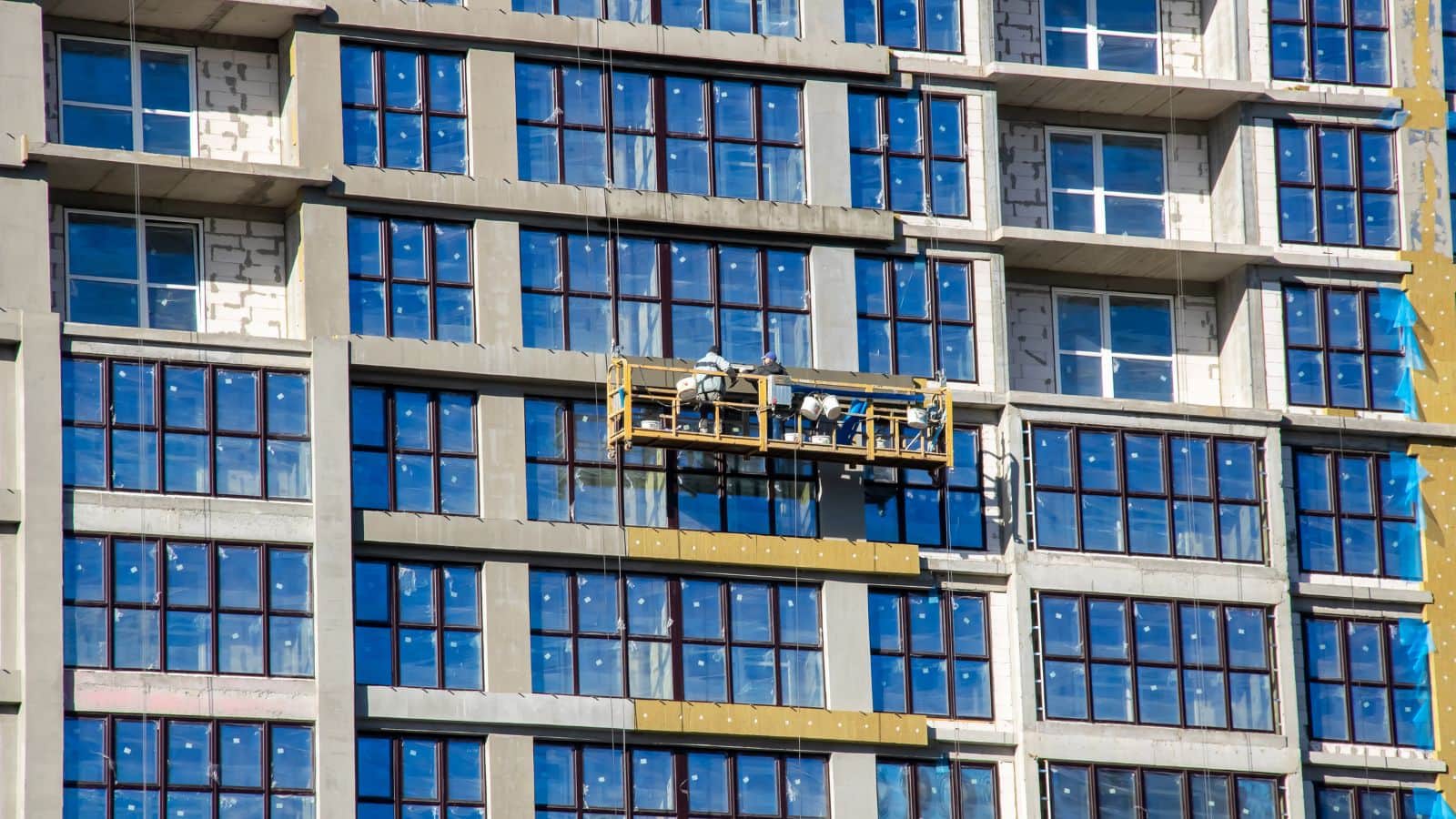 A worker on a mast climbing work platform cleaning the exterior windows of a high-rise building, demonstrating safety and efficiency in construction site management.