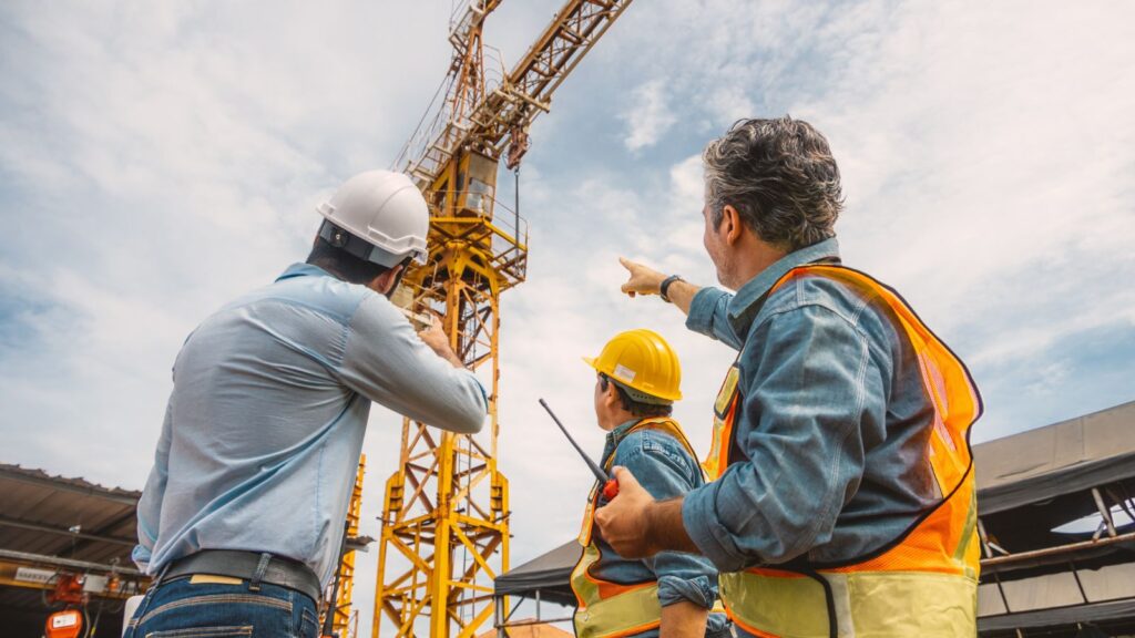 Construction engineers inspecting a tower crane with safety gear and a supervisor pointing during a site visit.