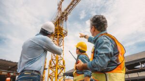 Construction engineers inspecting a tower crane with safety gear and a supervisor pointing during a site visit.