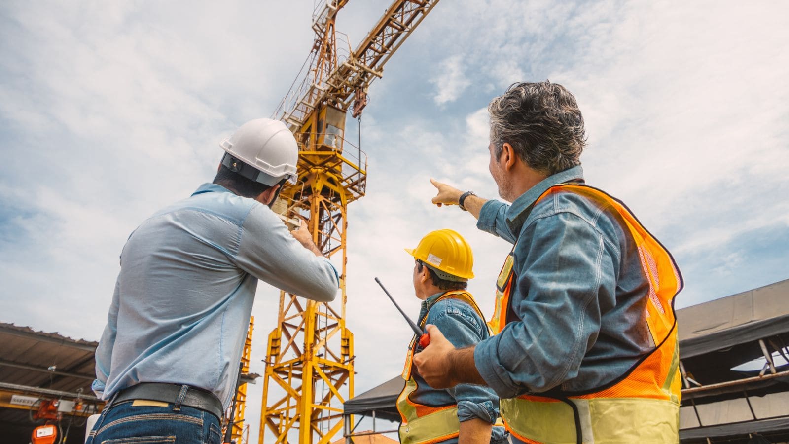 Construction engineers inspecting a tower crane with safety gear and a supervisor pointing during a site visit.