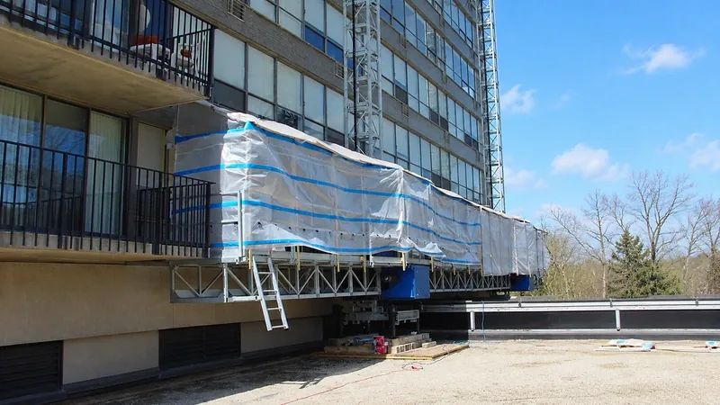 IHURMO single-mast climbing work platform wrapped in weather sheeting alongside an apartment block facade